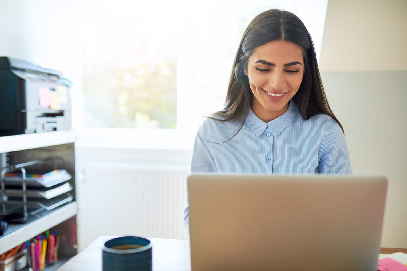 image of smiling woman in front of the laptop with the coffee mug next to her