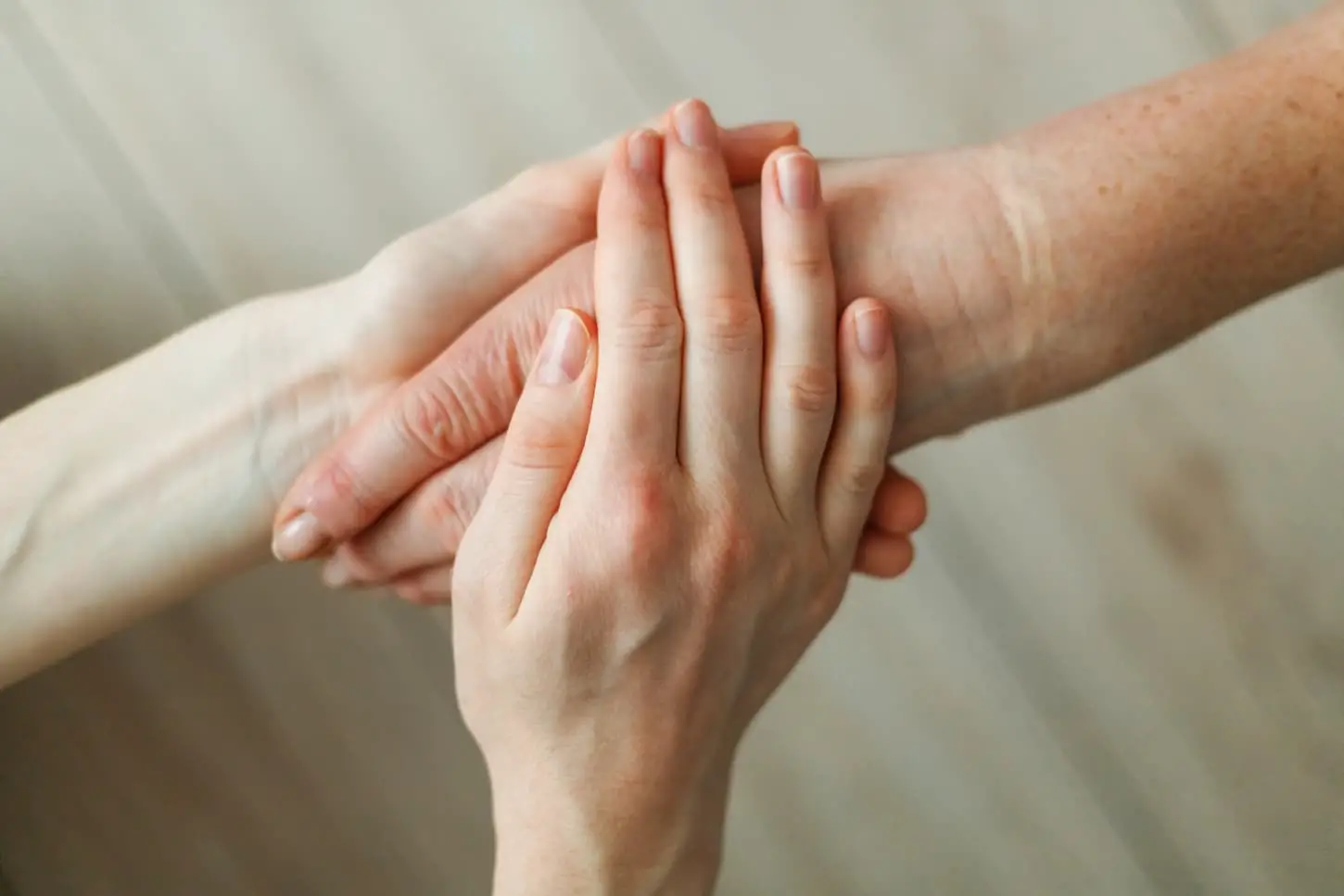 An image of a young girl's hand holding the hand of an elderly mother.