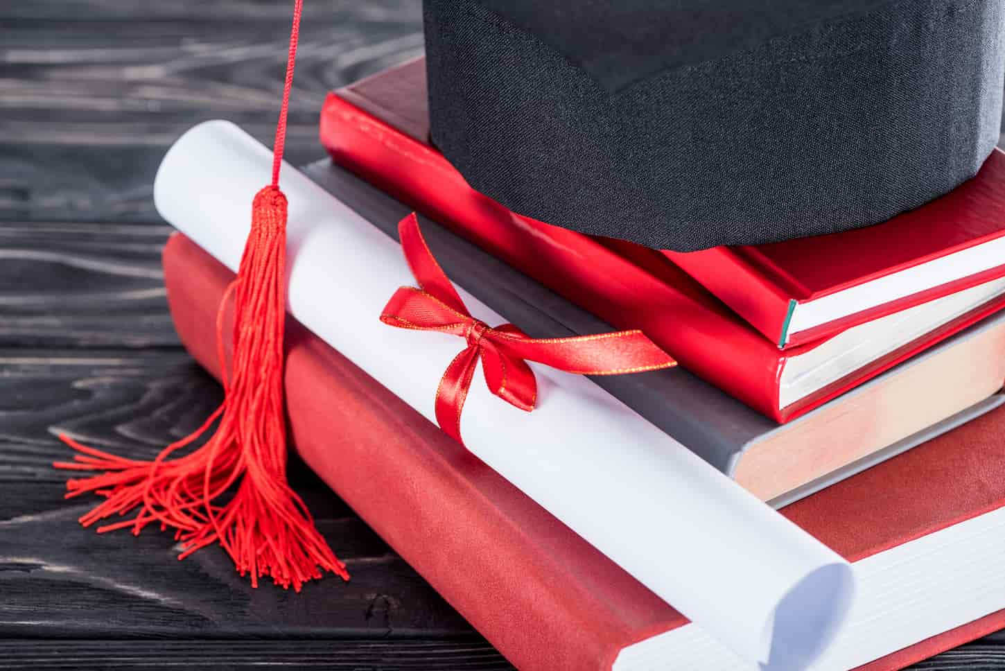 An image of the Graduation concept diploma and graduation cap on stack of books.